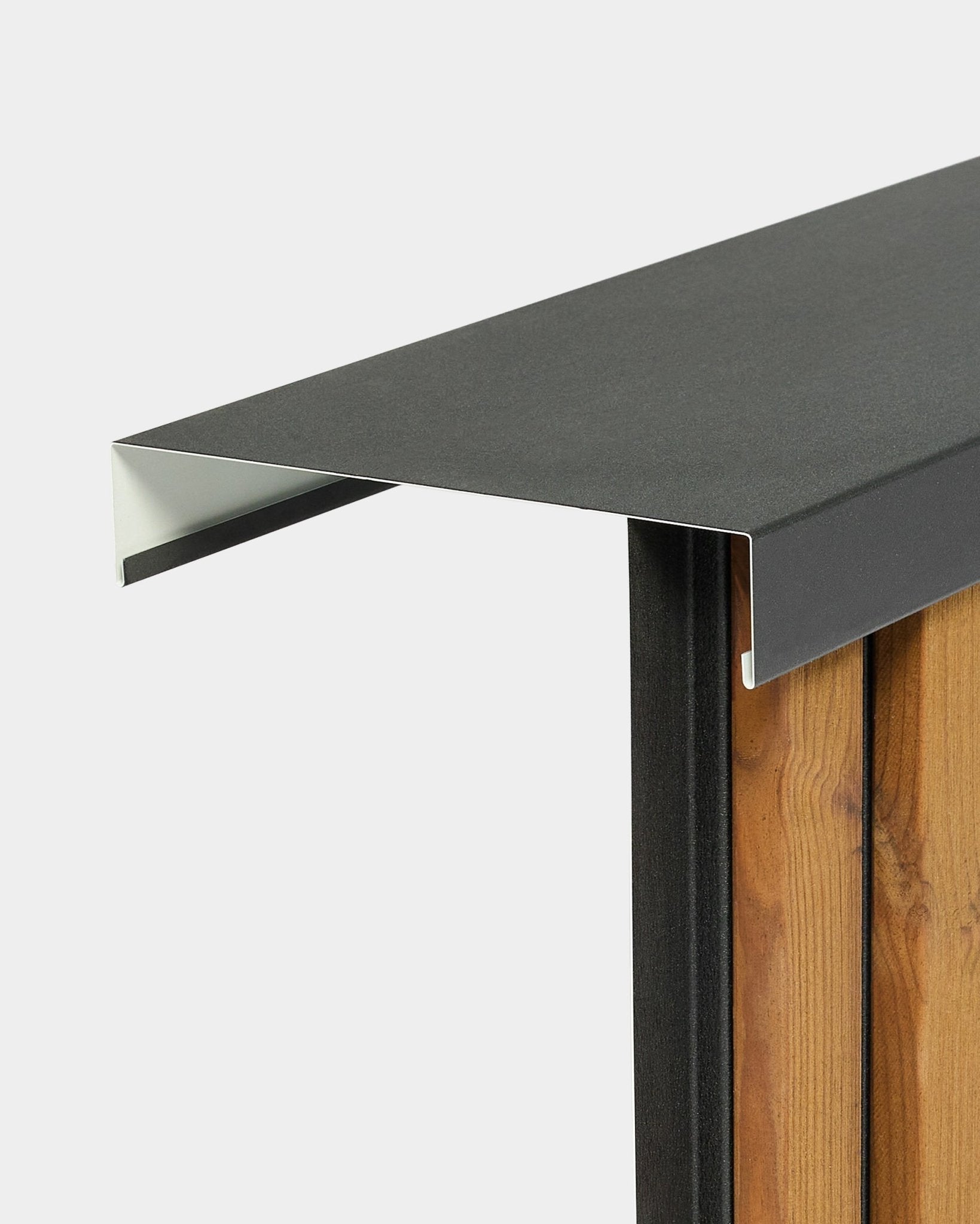WoodUpp Aluwood Level väggavtäckning (240 cm x 20 cm) sitter ovanpå ett trästaket och har en utåtgående profil i pulverlackerad aluminium black.